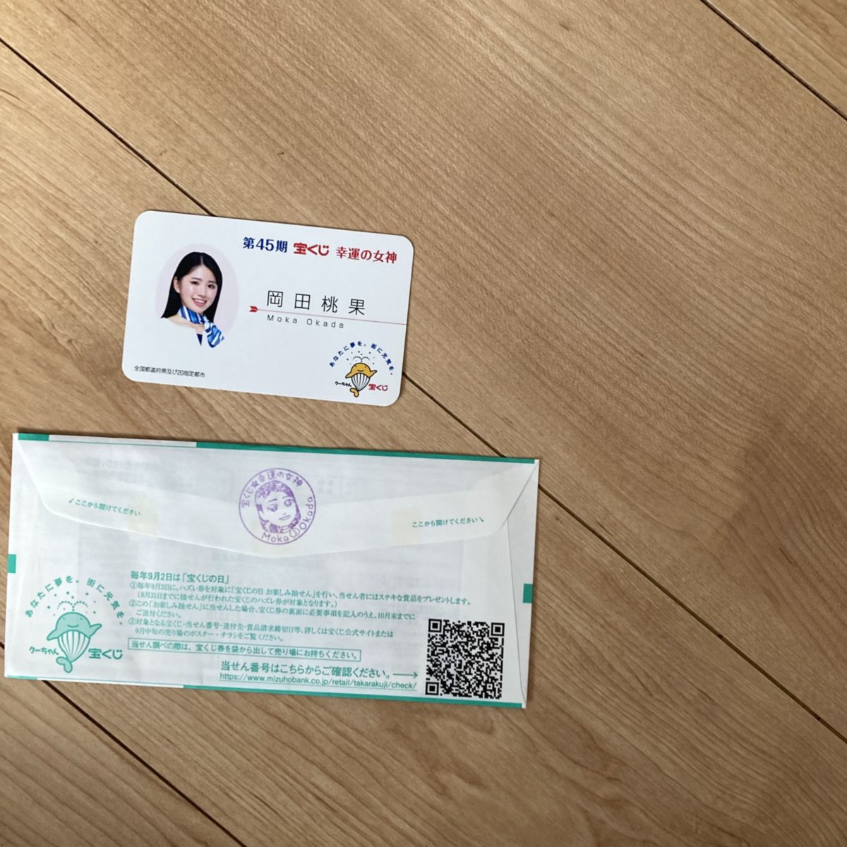 宝くじ幸運の女神「岡田桃果(おかだもか)」さんの名刺と女神のスタンプが押された宝くじの写真