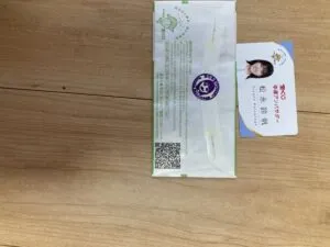 「写真の説明」Be My AI　木目のテーブルの上に、封筒と名刺が置かれています。名刺には女性の顔写真があり、以下のように書かれています。
宝くじ幸運アンバサダー「松永 鈴帆(まつなが すずほ)」