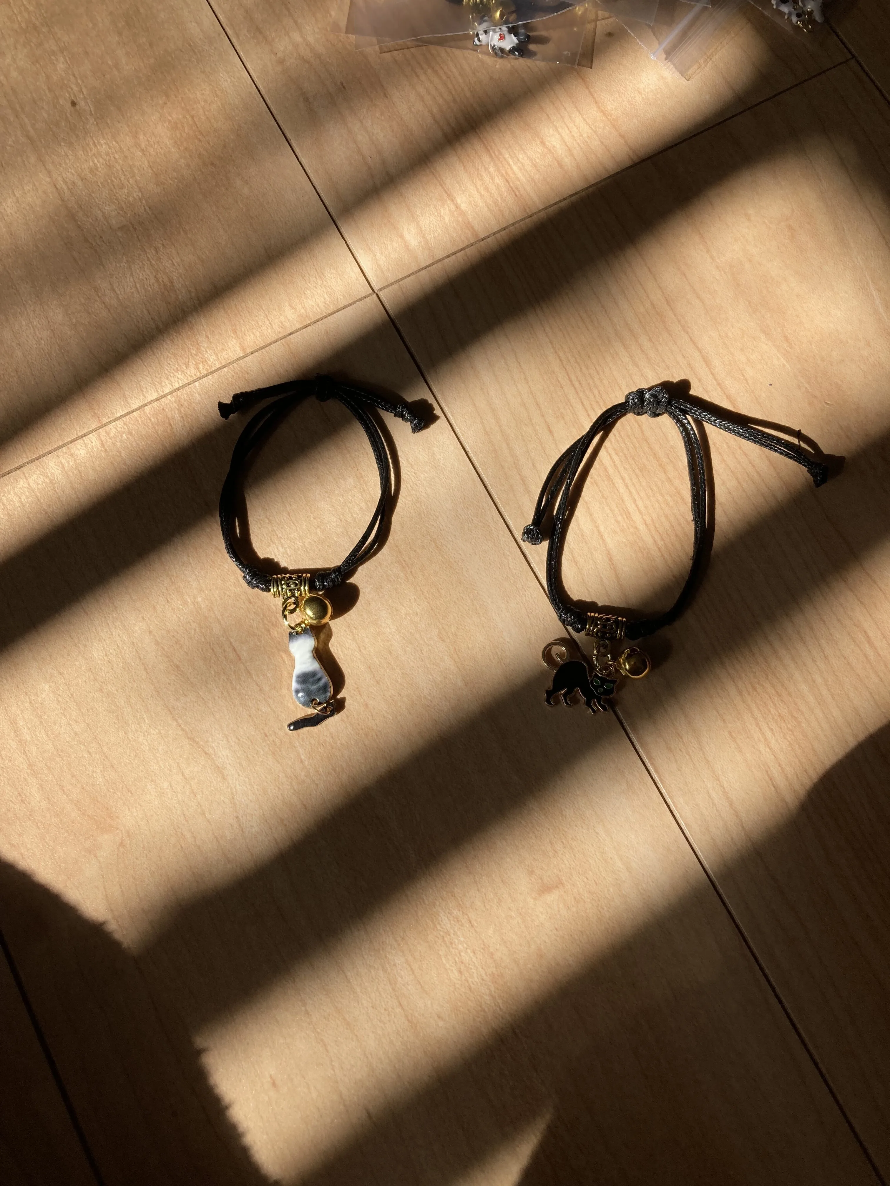 「写真の説明」ブレスレットが床に2個置かれてる。ブレスレットには猫のチャームと鈴が付いていて可愛い